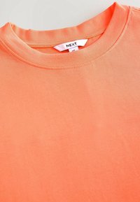 Kurzärmeliges T-Shirt mit Rundhalsausschnitt in einem hellen Korallton. Hergestellt aus glattem Baumwollstoff mit gleichmäßigen Nähten und einem Etikett mit dem Markennamen.