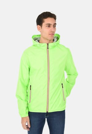 Uomo che indossa una giacca a cappuccio verde lime brillante con cerniera frontale e tasche laterali con cerniera, in piedi con una mano dietro la schiena.