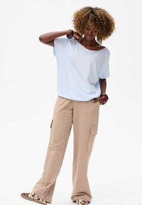 Lichtblauw oversized t-shirt met korte mouwen, gecombineerd met beige cargobroek met zijzakken, en bruine en witte schoenen met een patroon.