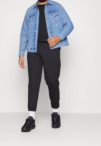 Chaqueta de denim en azul claro, camiseta negra con estampado, joggers negros ajustados y zapatillas negras con calcetines blancos. Un atuendo sencillo y casual.