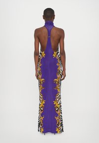 Lila Halfterneck-Kleid mit tiefem Rückenausschnitt, floralen und Zebramuster-Akzenten sowie einer schmalen, bodenlangen Silhouette.