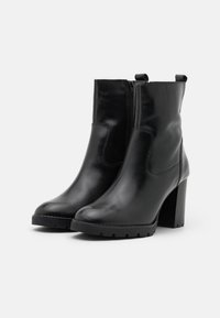 Botas de tobillo de cuero negro con punta redonda, cremallera lateral y un tacón alto y grueso. Textura suave con detalles de costura.
