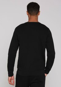 Sudadera negra con mangas largas, cuello redondo y puños y dobladillo acanalados, hecha de una tela suave y texturizada.