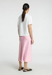 Chemise blanche à manches courtes, jupe midi rose pâle, et chaussures plates noires perforées. Texture lisse, design simple et coupe décontractée.