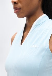 Ανοιχτό γαλάζιο αμάνικο αθλητικό τοπ με V-λαιμόκοψη, υφασμάτινες λωρίδες, λευκή επένδυση και μικρό λευκό λογότυπο στο αριστερό στήθος.