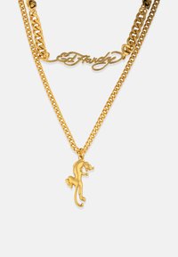 Złota podwójna naszyjnik łańcuszkowy z stylizowanym pendantem w kształcie lamparta oraz podpisaem w kursywie "Ed Hardy". Teksturowane ogniwa dodają szczegółu.