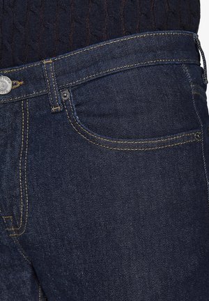 Jeans de mezclilla azul oscuro con cremallera, costura amarilla y diseño de cinco bolsillos. La tela tiene una textura suave con un ligero brillo.
