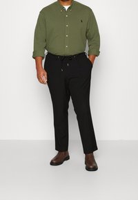 Zielona koszula zapinana na guziki z czarnymi spodniami z regulowanym sznurkiem, w połączeniu z brązowymi botkami za kostkę. Prosty design, prosta sylwetka.