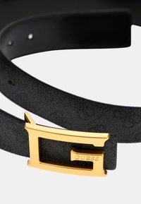Cinturón negro texturizado con una hebilla de metal en tono dorado, que presenta el nombre de la marca "GUESS" grabado. Diseño simple con acentos minimalistas.