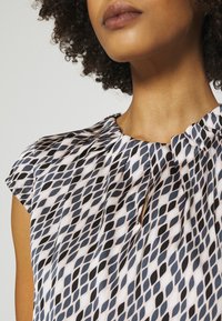 Bezrekawnik w wzorzystej tkaninie z motywem diamentu w czerni i różowym odcieniu blush, z delikatnymi zakładkami przy dekolcie.