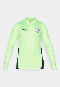 Langarm-Pullover aus fluorescentgrünem Material mit einem Viertelreißverschluss, dunkelblauen Seitenpaneelen und dem Manchester City-Logo auf der Brust.
