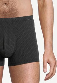 Torso maschile e parte superiore delle gambe che indossa boxer neri con un motivo esagonale e una cintura con marchio.