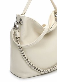 Kremowa skórzana torebka o fakturowanej powierzchni, z plecionym łańcuszkiem i metalowymi elementami ozdobnymi. Pojedynczy, regulowany pasek na ramię.