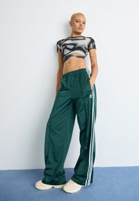 Black and gray abstract print crop top, green track pants with white stripes, and cream sneakers. Smooth fabric, relaxed fit, elastic waist.