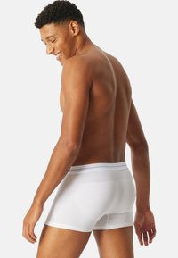 Vita bomullboxershorts med en strukturerad midjeband, figurnära design och slät yta. Sidan av shortsen visas för att framhäva bakprofilen.