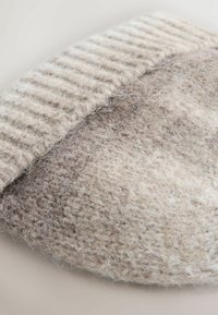 Close-up of beige knitted woolen fabric with visible soft fibers and ribbed edge detail.