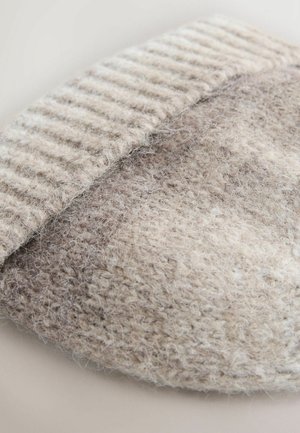 Tuvplāna skats uz beige krāsas adītu vilnas audumu ar redzamām mīkstām šķiedrām un ribotu maliņu.