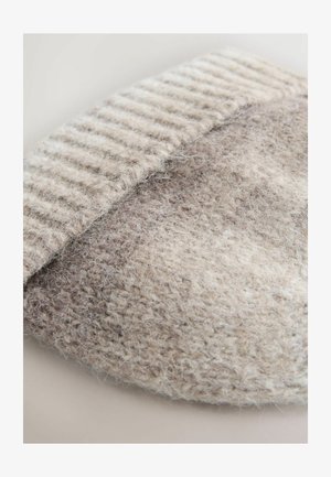 Lähetä lähellä beigeä neulevillakangasta, jossa näkyy pehmeät kuidut ja ribattu reuna.