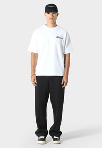 Witte T-shirt met korte mouwen met tekst en zwarte oversized broek. Zwarte pet met tekst. Schoenen zijn zwart met witte zolen. Eenvoudig, casual ontwerp.