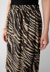 Schwarz-beige gestreifter Rock mit elastischem Bund und Kordelzug. Der Stoff wirkt glatt mit einem fließenden Design.