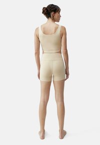 Beige idretts crop top og shorts sett, laget av glatt stoff, med en tettsittende design, brede stropper og sømløs konstruksjon.