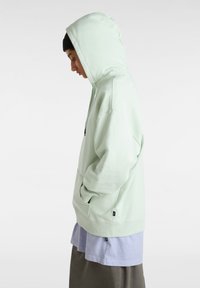 Light green hooded sweatshirt with a kangaroo pocket, ribbed cuffs, and a relaxed fit, layered over a light blue shirt and gray skirt.