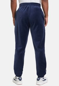 Marina blå fleece-joggingbyxor med elastiskt midjeband och muddar. Slät yta, sidofickor och en avslappnad passform. Matchas med vita sneakers.