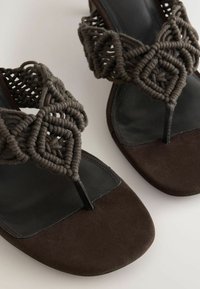 Brune lædersandaler med flettede macraméstropper og tåremdesign på en lys baggrund.