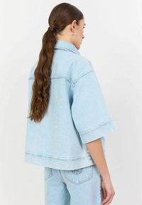 Svetlo modra kavbojka, kvadratnega dizajna, kratki rokavi, vidno šivanje in ravno rob. Združena z ustreznimi svetlo modrimi kavbojkami.