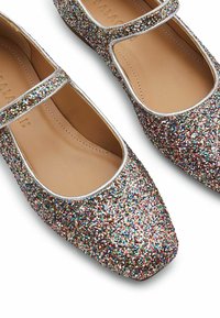 Paire de chaussures Mary Jane pailletées multicolores avec bordure argentée et semelles intérieures rembourrées beige, inclinées pour montrer les vues de dessus et de côté.