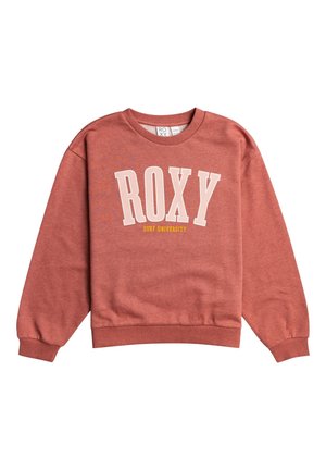 Femme portant un sweat-shirt rose poudré "ROXY Surf University", un pantalon de jogging gris et des baskets blanches avec des accents pastel. Mains dans les poches.