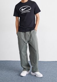 Černé bavlněné tričko s bílým logem Nike a textem, spárované se světle zelenými cargo kalhotami a bílými sportovními botami. Casual střih, minimalistický design.