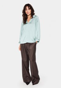 Blusa di raso blu chiaro con scollo a V e lunghe maniche a palloncino, abbinata a pantaloni a gamba larga marroni e scarpe nere a punta.