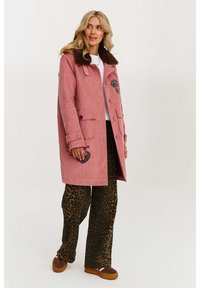 Ružový kordurový kabát s hnedým kožušinovým golierom, dvoma prednými vreckami, vyšívanými detailmi a purpurovými gombíkmi, kombinovaný s nohavicami v leopardom vzore.