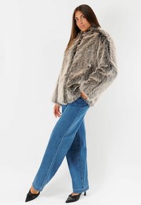 Giacca in pelliccia sintetica nei toni grigio e beige, caratterizzata da un colletto alto e tasche laterali. Abbinata a jeans in denim blu a vita alta e tacchi neri.