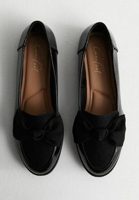 Ballerine nere con finitura lucida in pelle verniciata e punta in morbido suede, caratterizzate da un dettaglio in tessuto a forma di fiocco sul fronte e suole ammortizzate.