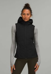 Gilet nero con cappuccio, zip, design trapuntato e tasche laterali, indossato sopra una maglietta a maniche lunghe grigia chiara. Tessuto strutturato con una vestibilità sportiva.