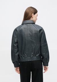 Donkergrijs leren bomberjack met een gestructureerde afwerking, geribbelde manchetten en een geplooide tailleband. Met kraagontwerp en raglanmouwen.