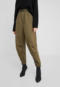 Olijfgroene joggingsbroek met een elastische tailleband en trekkoord. Voorzien van zijzakken en elastische boorden. Katoenen mix stof, zachte textuur.
