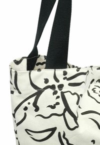 Torba tote z płótna w białym kolorze z czarnym wzorem kwiatowym. Posiada solidne czarne uchwyty oraz zwięzły, strukturalny kształt.