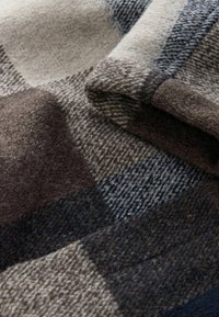 Soft folded wool fabric with large check pattern in beige, brown, and navy blue tones showcasing texture and weave detail.