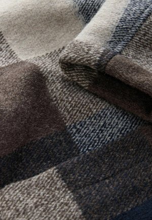 Soft folded wool fabric with large check pattern in beige, brown, and navy blue tones showcasing texture and weave detail.