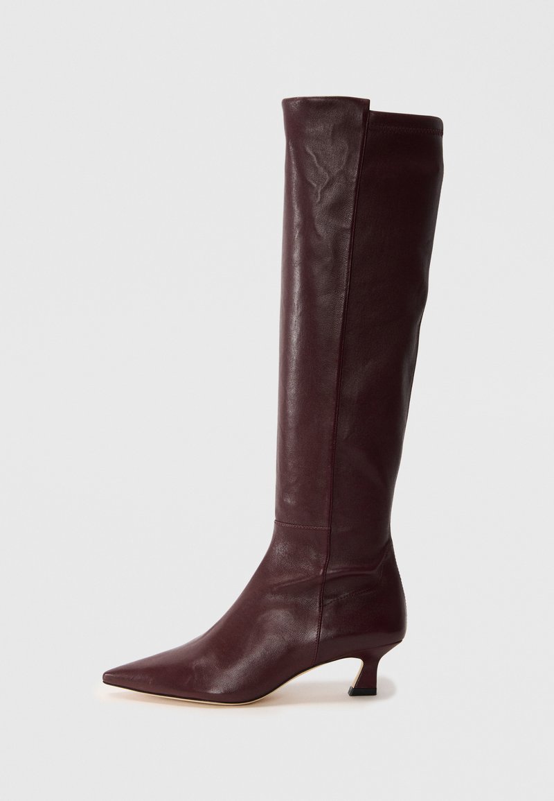 Burgundy leather knee-high boot with a pointed toe and slim kitten heel. Smooth texture with minimal detailing and a fitted silhouette.