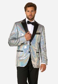 Holografická flitrová smokingová bunda s čiernymi saténovými klopami, jedným gombíkom na zapínanie a dvoma prednými vreckami. Nosená cez bielu košeľu a motýlik.