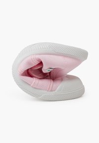 Rosa Stoffschuh mit strukturierter Oberfläche, flexiblem Design und weißer Gummisohle, die eine hohle Form zeigt.