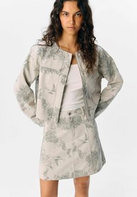 Ensemble veste et jupe en tissu gris clair avec un motif floral. La veste présente un col rond et un design court, tandis que la jupe est ajustée.