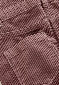 Kordurovina v barvi prašno rože, z navpično rebrasto teksturo in vidnimi žepi z detajli zgornjega šiva.