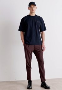 Μαύρο φανελένιο t-shirt, σκούρο καφέ παντελόνι κομμένα, μαύρο καπέλο, μαύρα παπούτσια; μινιμαλιστικός σχεδιασμός χωρίς ορατά μοτίβα ή παρεμβολές.