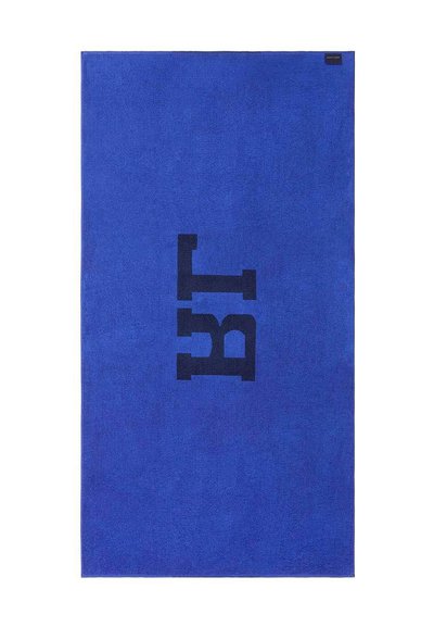 Μπλε ορθογώνια πετσέτα με μεγάλες μαύρες γράμματα "BT" στο κέντρο και μια μικρή μαύρη ετικέτα στην πάνω δεξιά γωνία.