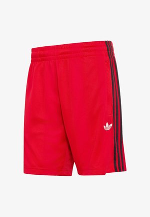 Shorts de sport rouges avec taille élastique, bandes latérales noires et logo trefoil blanc d’Adidas sur la jambe gauche.